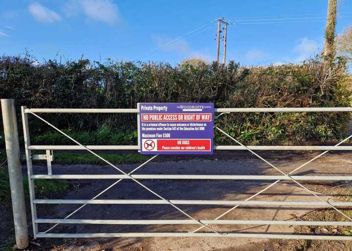 Metal gate with a 'No Public Access' sign attached, surrounded by greenery and a clear blue sky.