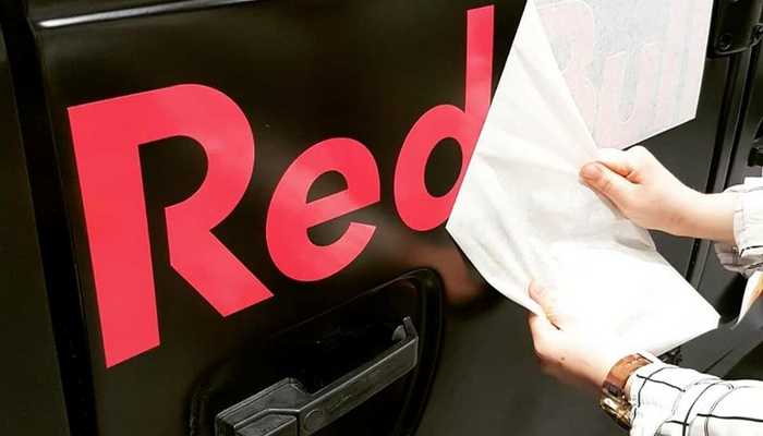 Someone peeling away contact paper revealing vinyl logo on vehicle