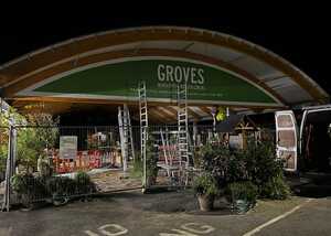 Nighttime image of a garden center entrance with ladders and greenery. Sign reads "GROVES."