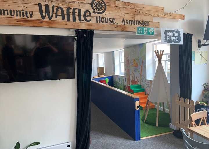Interior of a community space with a wooden sign reading "Waffle House" and colorful play area.