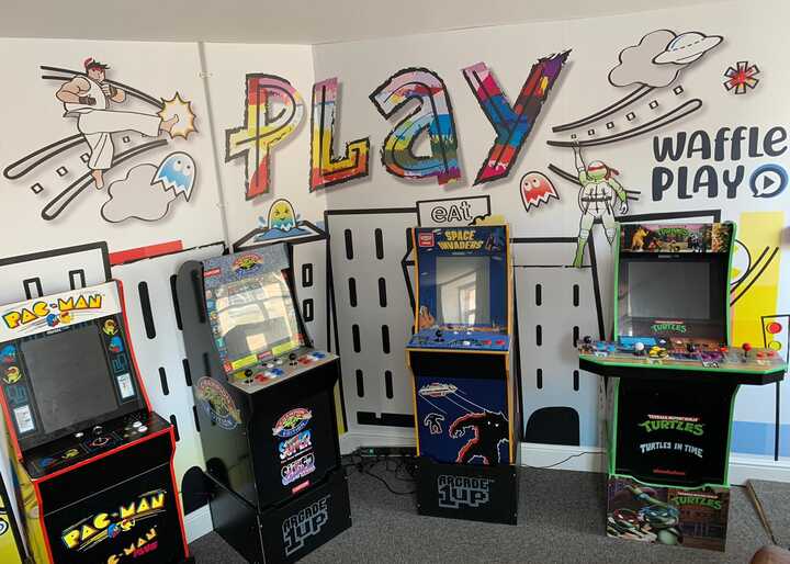 Arcade games in a colorful room with "PLAY" mural on the wall.