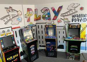 Arcade games in a colorful room with "PLAY" mural on the wall.