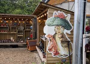 Garden display featuring Benjamin Bunny statue and potted plants, with rustic wooden structures.