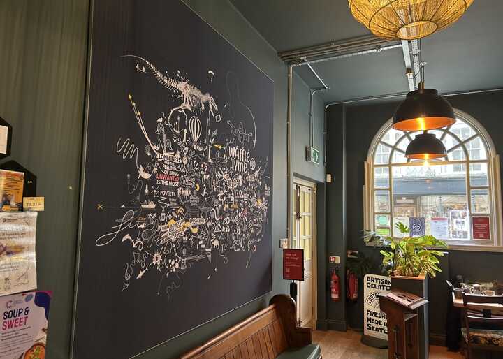 Interior of a cafe with a large mural, a window, and a hanging light fixture.