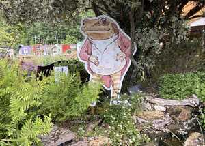 Jeremy Fisher artwork display stands by a pond, surrounded by greenery.
