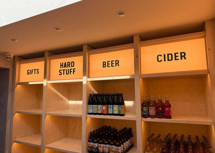 Shelves with signs labeled "GIFTS," "HARD STUFF," "BEER," and "CIDER," holding various beverages.