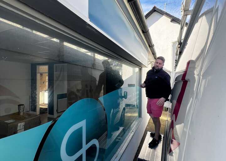 A person stands between two buildings, one with a large blue Sonder logo, under a clear sky.