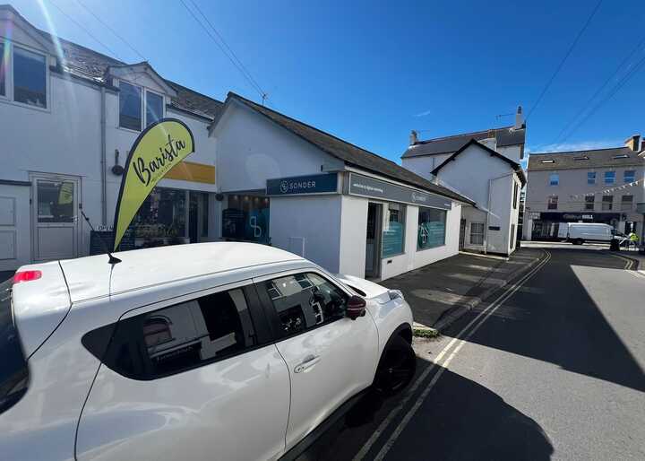 A white vehicle parked near a building with a yellow banner in bright sunlight.