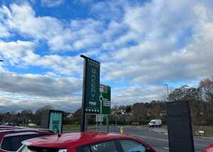 Outdoor Rise Bakery signage with directional information, cloudy blue sky, and parked cars in view.