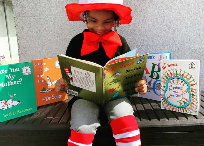 Young girl dressed in stripey socks and hat reading Dr.Seuss Books
