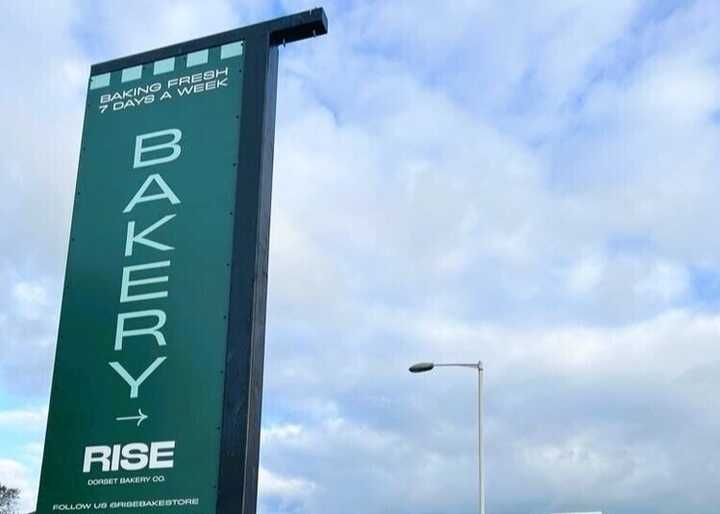 Sign for "BAKERY" with the word "RISE" below, against a cloudy sky.