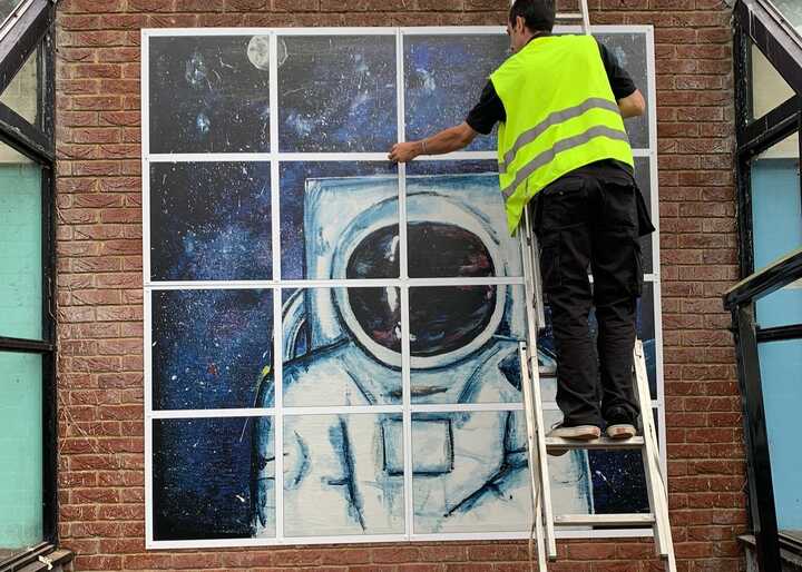 A person in a safety vest is installing wall graphic of an astronaut in 16 individual panels