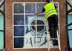 A person in a safety vest is installing wall graphic of an astronaut in 16 individual panels