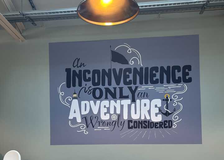 Text on a wall reads, "An inconvenience is only an adventure wrongly considered."