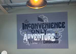 Text on a wall reads, "An inconvenience is only an adventure wrongly considered."